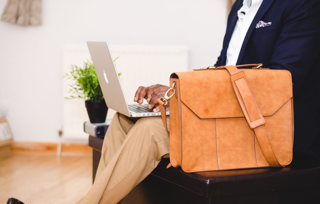 Pessoa sentado com um Macbook no colo e uma bolsa tipo carteiro ao seu lado pesquisando sobre sociedade unipessoal.