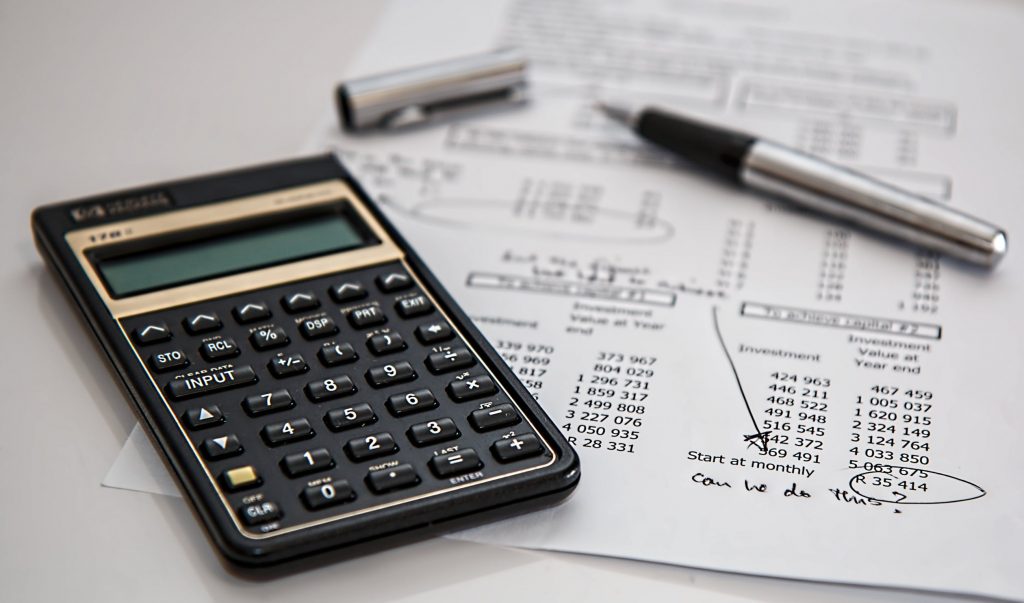 imagem de uma calculadora, uma caneta e algumas contas: importantes para o calculo de quais impostos uma microempresa paga.
