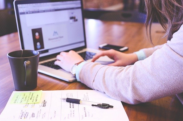 planejamento e organização nas atividades de trabalho de uma mulher acessando à internet, uma caneca preta e uma caneta