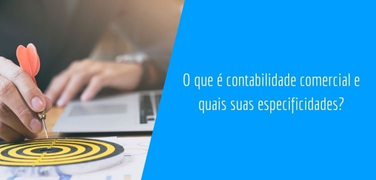 imagem retangular com sobreposição de um trapézio azul a direita, com o título da matéria "o que é contabilidade comercial e quais suas especificidades". Na parte esquerda, é possível ver duas mãos ,uma está segurando um dardo vermelho logo acima de um alvo redondo, com círculos intercalados entre preto e amarelo. Ao fundo, desfocado, temos um notebook e parte de um tórax feminino.