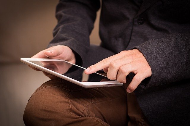 homem branco segurando um tablet e teclando em cima