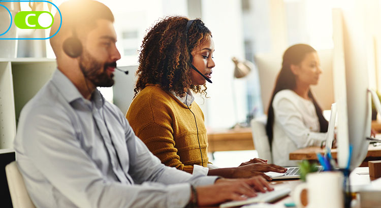 Na imagem, duas pessoas trabalhando em frente ao computador, com fones de ouvido e mirofones. Como se estivessem em um telemarketing.