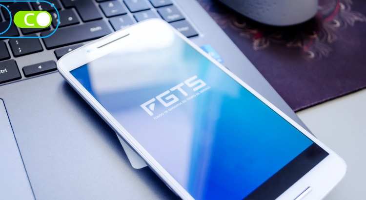Na foto um celular com o logotipo do FGTS na tela, ele está apoiado e, cima de um notebook.